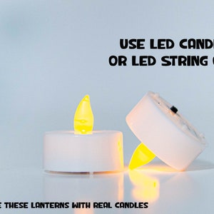 May include: Two white LED tea lights with a yellow flame. The text "USE LED CANDLE OR LED STRING ONLY" is above the lights. The text "DO NOT USE THESE LANTERNS WITH REAL CANDLES" is below the lights.