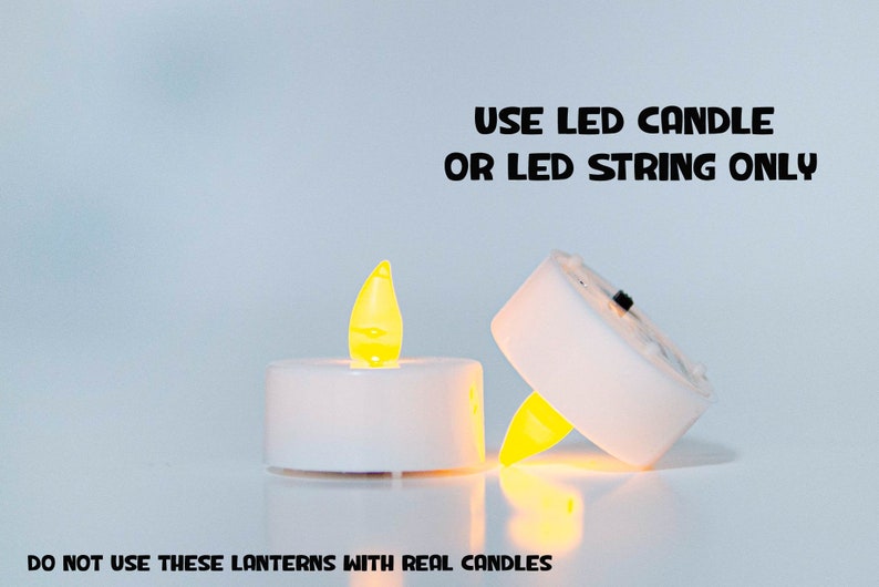 May include: Two white LED tea lights with a yellow flame. The text "USE LED CANDLE OR LED STRING ONLY" is above the lights. The text "DO NOT USE THESE LANTERNS WITH REAL CANDLES" is below the lights.