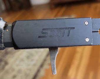 May include: A black metal tool with the word "SCOTT" engraved on the top. The tool has a lever and a pair of jaws.