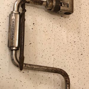 May include: A vintage silver Craftsman hand drill with a wooden handle. The drill has a metal crank and a chuck for holding drill bits.