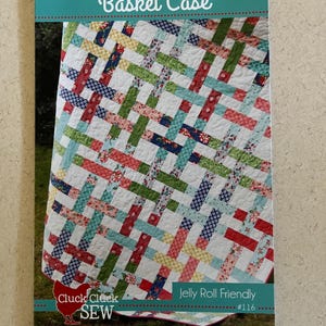 May include: A quilt pattern book titled "Basket Case" featuring a colorful quilt design. The quilt has a woven pattern with red, green, blue, and floral fabric strips. The book also includes the text "Jelly Roll Friendly" and the logo "Cluck Cluck Sew".
