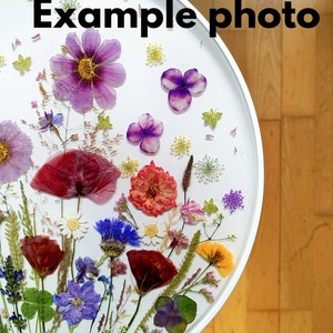 Puede incluir: Una mesa redonda blanca con una variedad de flores y hojas prensadas incrustadas en resina transparente. Las flores son de color rosa, morado, rojo, amarillo y blanco.