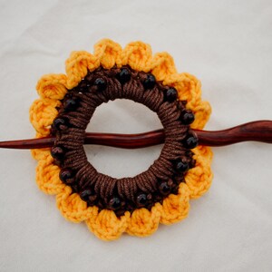 Puede incluir: Una pinza para el pelo de girasol de ganchillo marr&oacute;n y amarillo con cuentas marrones y un palo de madera.