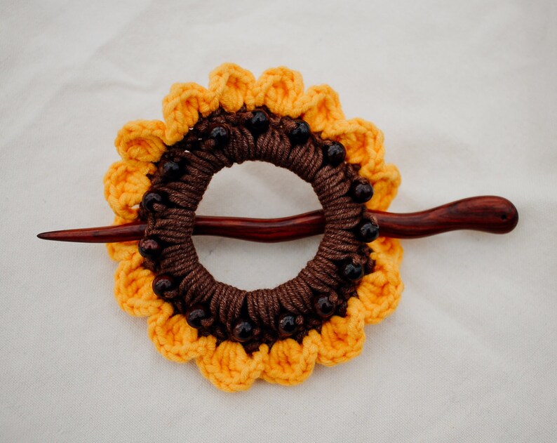 Puede incluir: Una pinza para el pelo de girasol de ganchillo marr&oacute;n y amarillo con cuentas marrones y un palo de madera.