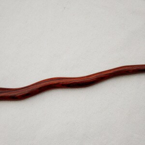 Puede incluir: Un palo de pelo largo y delgado de madera roja oscura con un mango curvo. El palo tiene un patr&oacute;n de veta de madera natural.