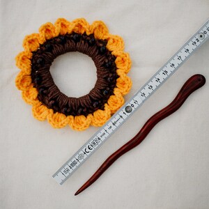 Puede incluir: Un scrunchie para el pelo de girasol tejido a crochet con cuentas marrones y una varita para el pelo de madera.
