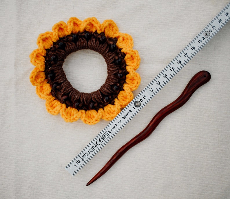 Puede incluir: Un scrunchie para el pelo de girasol tejido a crochet con cuentas marrones y una varita para el pelo de madera.