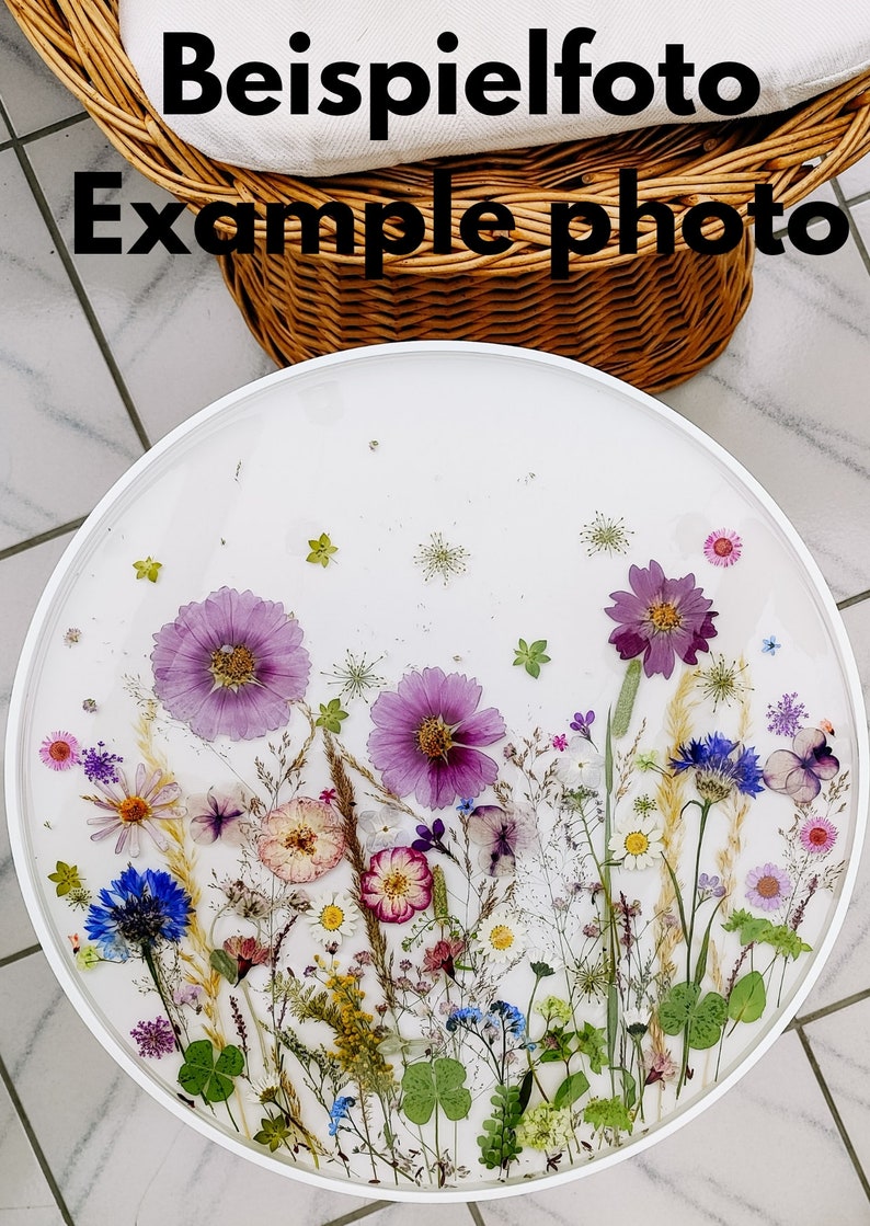 Puede incluir: Una mesa redonda blanca con una capa de resina transparente que presenta flores y vegetaci&oacute;n prensadas. Las flores son moradas, rosas, blancas, azules y amarillas. La mesa est&aacute; rodeada por un marco blanco.