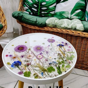 Puede incluir: Mesa auxiliar redonda blanca con patas de madera. La tapa de la mesa est&aacute; hecha de resina transparente con flores y hojas prensadas. El texto "Beispielfoto Example photo" est&aacute; impreso debajo de la mesa.