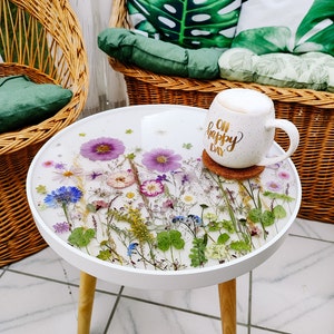 Puede incluir: Mesa auxiliar redonda blanca con base de madera. La superficie de la mesa est&aacute; decorada con flores y vegetaci&oacute;n prensadas. Una taza blanca con el texto "Oh Happy Day" est&aacute; sobre la mesa.
