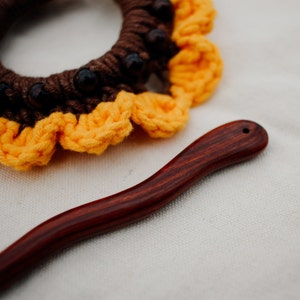 Puede incluir: Un scrunchie para el pelo de color marr&oacute;n y amarillo tejido a crochet con cuentas marrones y un palo para el pelo de madera oscura.