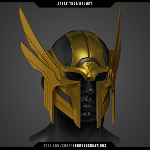 Puede incluir: Un casco espacial dorado y negro con un diseño alado. El casco tiene una visera y un símbolo en la parte delantera.