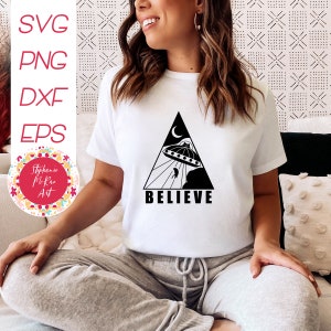 May include: A white t-shirt with a black triangle design featuring a UFO, a crescent moon, and the word "BELIEVE".