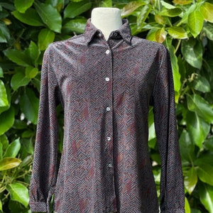 Op de afbeelding: Een lang mouw overhemd met knopen en een zwart, bruin en rood chevron patroon.