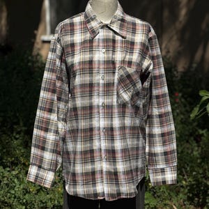 May include: A long-sleeved plaid shirt with a black, white, red, and beige plaid pattern. The shirt has a button-down collar and a single chest pocket.