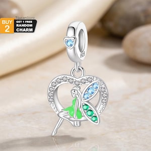Puede incluir: Un charm de plata con un diseño de hada. El charm presenta un marco en forma de corazón con cristales transparentes, un hada con un vestido verde y detalles azules y verdes. El charm tiene un pequeño corazón azul en la parte superior y está marcado con "S925".