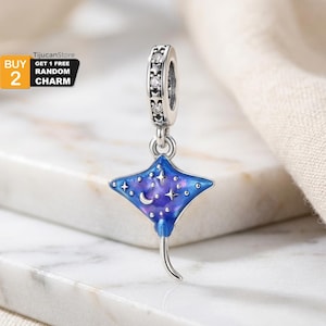 May include: A silver charm with a blue and purple stingray design. The charm features a starry night sky pattern with a crescent moon and stars. The charm is suspended from a silver ring with clear stones.