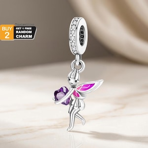 Puede incluir: Un charm de plata con una hada sosteniendo un corazón morado. El hada tiene alas rosas y moradas y está unida a un anillo con piedras transparentes. Este charm tipo colgante es probablemente para una pulsera o collar.