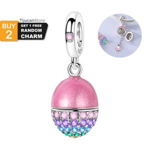 May include: A silver charm with a pink, glittery, egg-shaped pendant. The bottom half of the pendant is adorned with a row of colorful, sparkling gemstones. The charm has a small pink gem on the top loop. The image also includes text that says "BUY 2 GET 1 FREE RANDOM CHARM".
