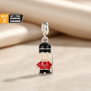 May include: A silver charm depicting a British Royal Guard in a red coat, black hat, and black pants. The charm has a smiling face and holds a silver rifle. The charm is suspended from a silver loop.