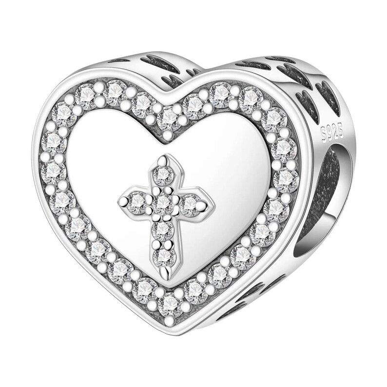 May include: A silver heart-shaped charm with a cross design. The charm features a heart outline with a border of small, clear gemstones. Inside the heart is a cross, also adorned with gemstones. The charm is likely made of sterling silver.