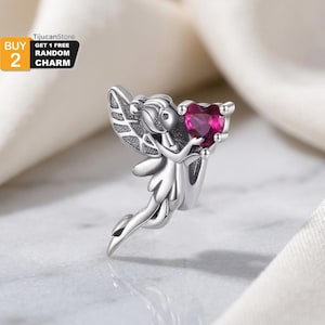 Puede incluir: Un charm de plata que representa un hada sosteniendo un corazón de piedra preciosa rosa intenso. El hada tiene alas detalladas y un vestido fluido. El charm está diseñado para ser un colgante o una cuenta para una pulsera o collar.