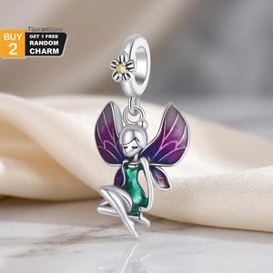 Puede incluir: Un charm de hada plateado con un acento floral. El hada tiene alas moradas y verdes y está sentada. El charm está diseñado para ser añadido a una pulsera o collar. La imagen también incluye el texto "BUY 2 GET 1 FREE RANDOM CHARM".