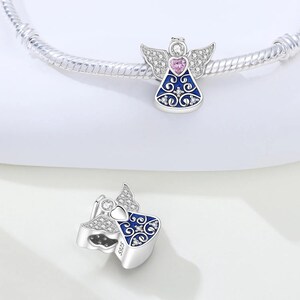 May include: Silver angel charm with a blue dress, pink heart, and crystal accents. The charm has detailed wings and is designed to be added to a bracelet. The charm is a decorative jewelry item.