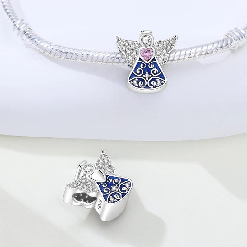 May include: Silver angel charm with a blue dress, pink heart, and crystal accents. The charm has detailed wings and is designed to be added to a bracelet. The charm is a decorative jewelry item.