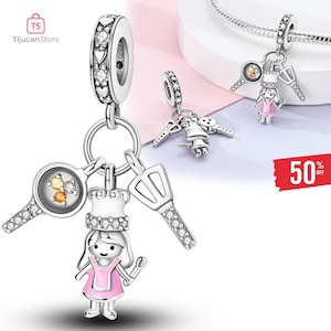 May include: Silver charm with a chef design, including a chef figure in a pink dress, a frying pan, and a spatula. The charm also features a key and a small figure with keys. The charm is adorned with clear crystals.