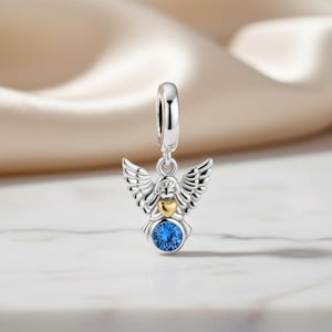 May include: A silver angel charm with detailed wings, a gold heart, and a large, round blue gemstone. The charm has a loop at the top for easy attachment to a bracelet or necklace. The angel charm is a symbol of protection and love.