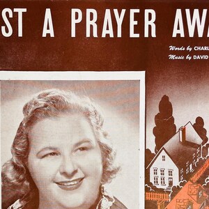 May include: A vintage sheet music cover with the title "Just a Prayer Away" in large white letters. The cover features a black and white photo of a woman with a warm smile. The text "Words by Charles Tobias" and "Music by David Kapp" is printed below the photo.
