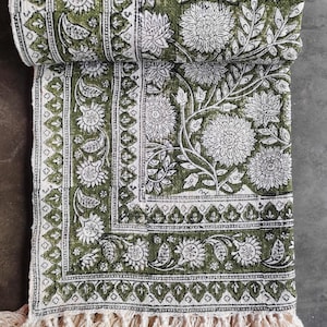 May include: A folded green and white floral patterned textile with a cream fringe. The design features large white flowers and leaves on a green background. The edges have a detailed border.