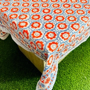 May include: A blue and white tablecloth with a red floral pattern. The tablecloth is made of cotton and has a fringed edge.