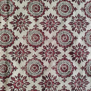 May include: A white fabric with a repeating pattern of red and black floral designs. The fabric has a textured surface.