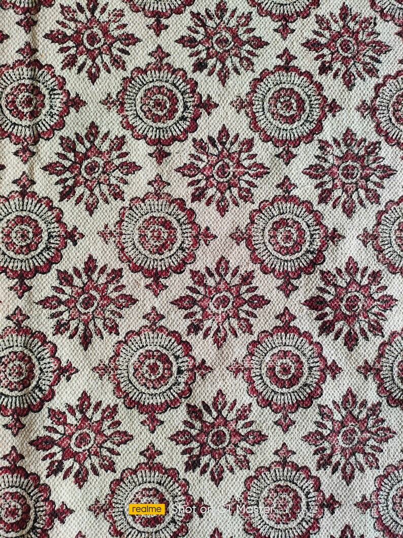 May include: A white fabric with a repeating pattern of red and black floral designs. The fabric has a textured surface.