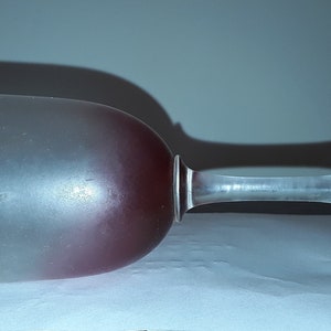 Puede incluir: Una copa de vino de vidrio esmerilado con una base teñida de rojo. La copa está tumbada de lado sobre una superficie blanca.