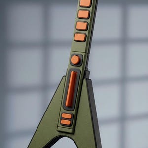May include: A stylized, olive green guitar-shaped object with orange accents. The design features a series of rectangular buttons and a central orange bar. The guitar has a V-shaped body and a rectangular neck.
