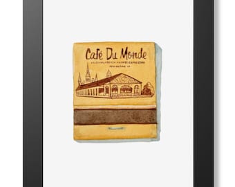 May include: A framed print featuring a yellow matchbook cover with a brown illustration of the Cafe Du Monde building in New Orleans. The text reads Cafe Du Monde, Original French Market Coffee Stand, New Orleans, LA. The frame is black and rectangular.
