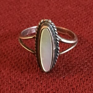 May include: A silver ring with an oval-shaped mother-of-pearl stone set in a silver bezel. The ring has a delicate, twisted band.