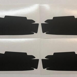 May include: Four black vinyl decals for car headlights. The decals are shaped like a curved line with a small bump on the top.