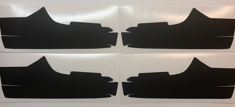 May include: Four black vinyl decals for car headlights. The decals are shaped like a curved line with a small bump on the top.