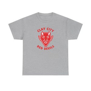 May include: A heather grey short-sleeved t-shirt featuring a red graphic of a devil face centred on the chest. Above the devil face is the text CLAY CITY in red, and below the devil face is the text RED DEVILS in red, all in a bold font.