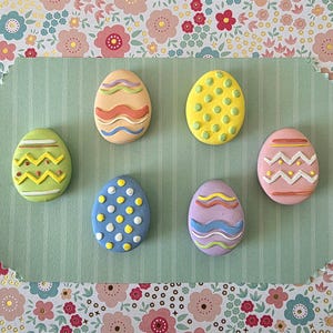 Puede incluir: Siete huevos de Pascua decorativos de colores. Cada huevo es de un color diferente, incluyendo verde, amarillo, rosa, azul, beige y morado. Los huevos están decorados con varios patrones, como zigzags, puntos y líneas onduladas.