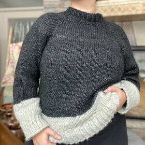 May include: A black and white knit sweater with a mock neck and long sleeves. The sweater has a contrasting white band at the bottom of the sleeves and the bottom of the sweater.