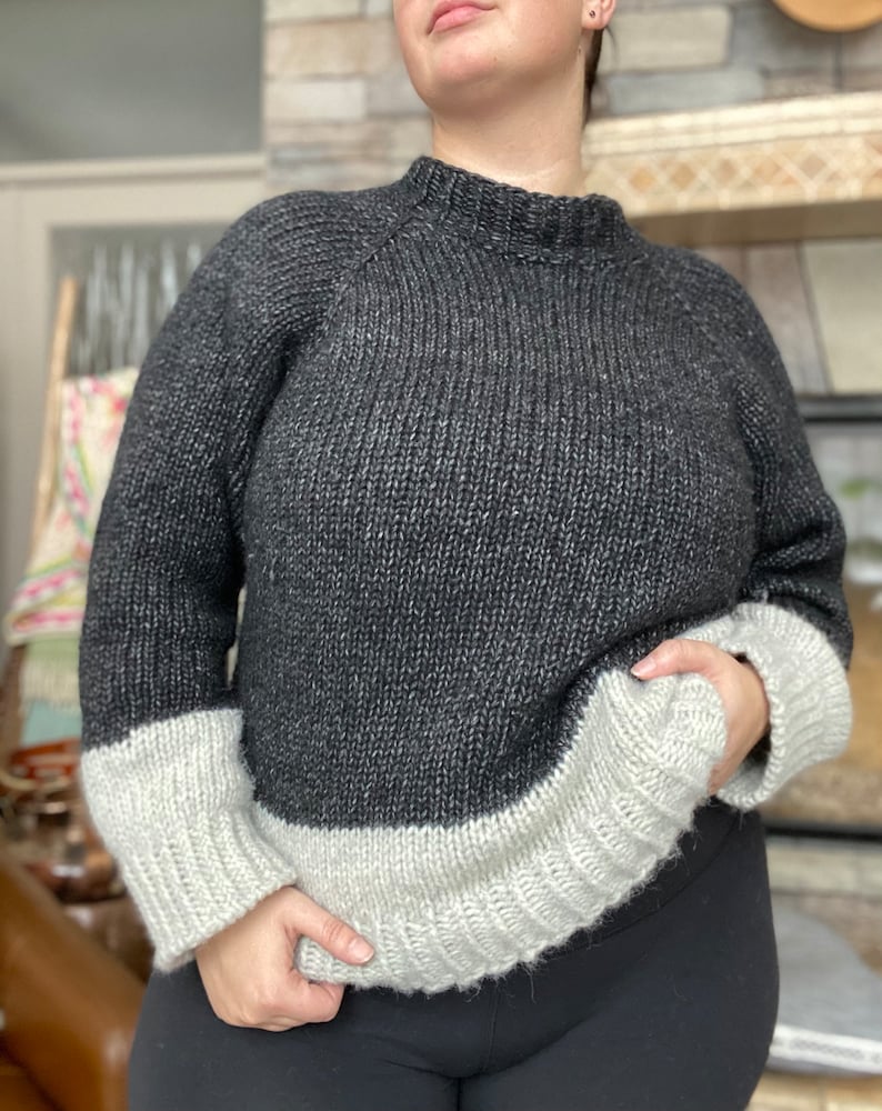 May include: A black and white knit sweater with a mock neck and long sleeves. The sweater has a contrasting white band at the bottom of the sleeves and the bottom of the sweater.