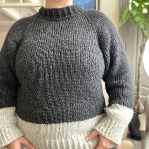 May include: A gray and white knit sweater with a mock neck and long sleeves. The sweater has a contrasting white band at the bottom and cuffs.
