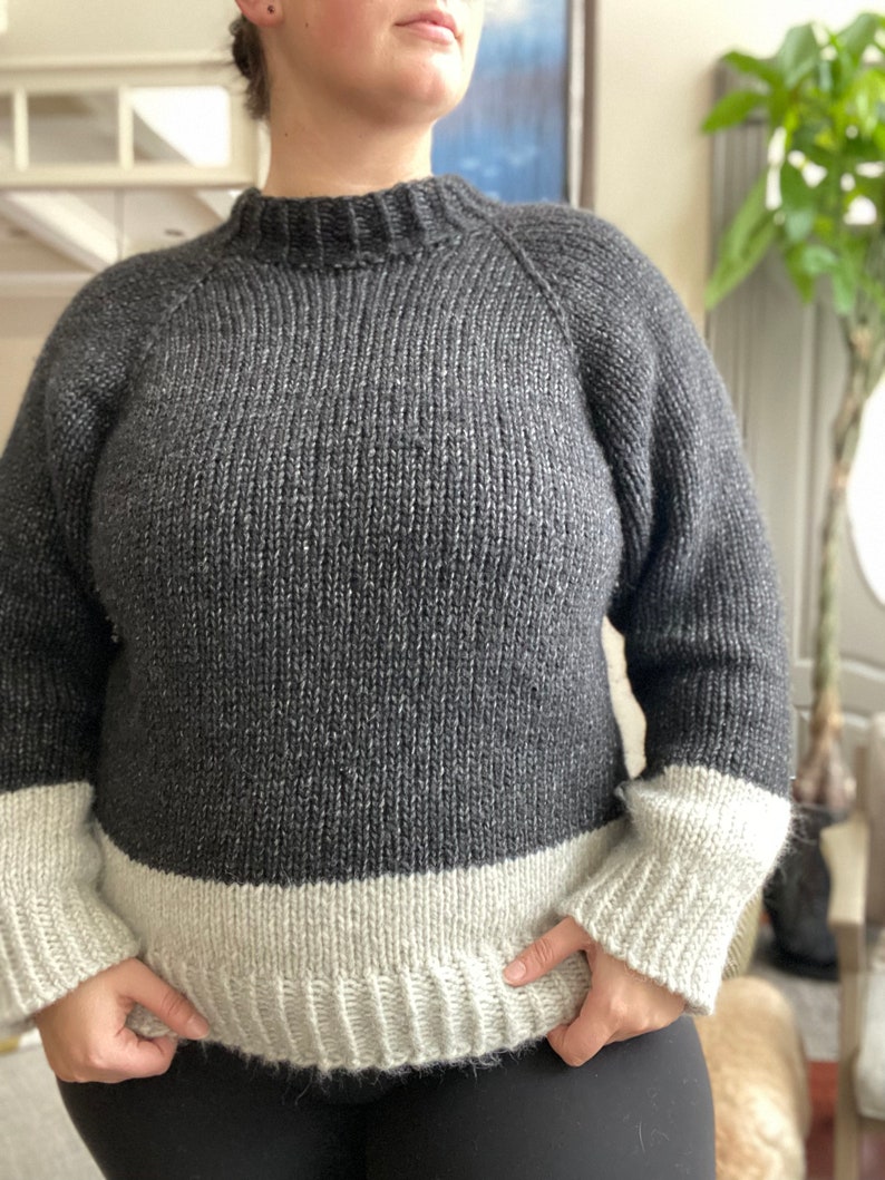 May include: A gray and white knit sweater with a mock neck and long sleeves. The sweater has a contrasting white band at the bottom and cuffs.