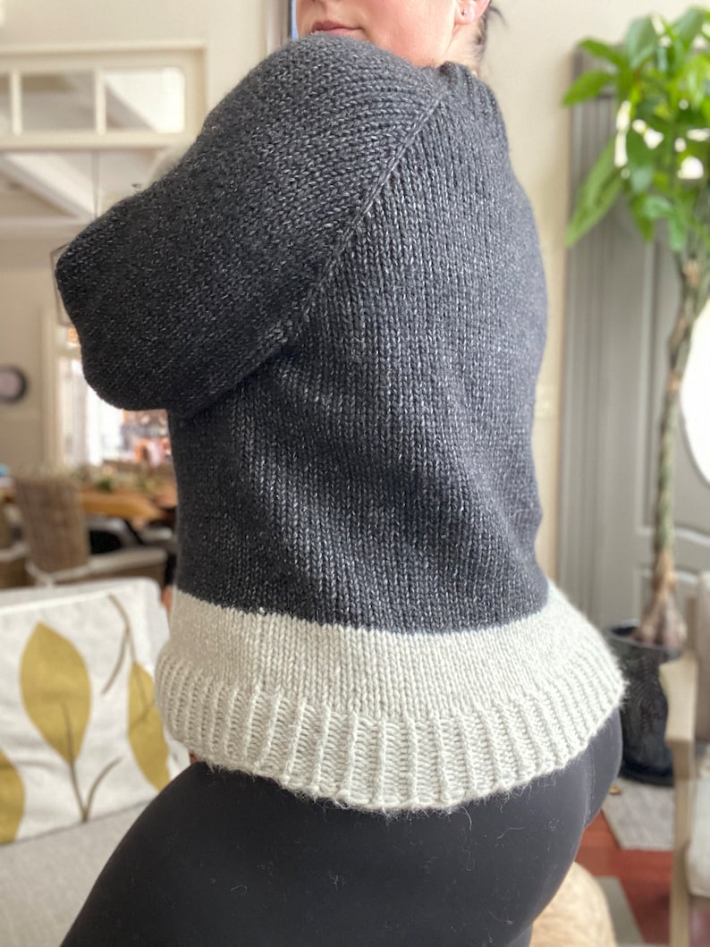 May include: A black and white knit sweater with a ribbed hem. The sweater is made of a soft, textured yarn.