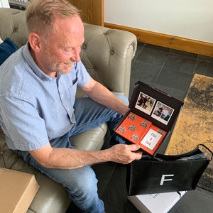 K&ouml;nnte beinhalten: Eine Person &ouml;ffnet eine schwarze Box mit einem roten und wei&szlig;en gemusterten Papier darin. Die Box enth&auml;lt eine Reihe von Fotos und eine Karte mit der Aufschrift "Print A Stack".